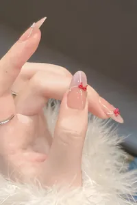 Detailed view of long almond press-on nails with nude pink cat-eye and red ribbon bow