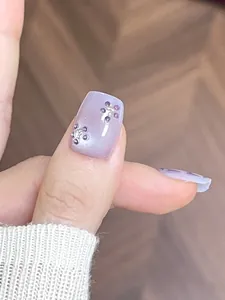 Detailed macro view of short square purple press-on nails with 3D floral rhinestone decor