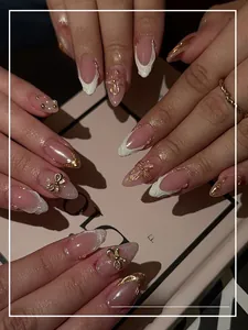 Detail of pink gradient press-on nails with 3D gold bows and pearl accents