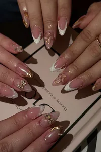 Close-up of pink press-on nails with 3D bows, white French tips and pearl accents