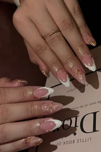 Detail of luxury almond fake nails with pink base, gold relief flower and white pearls