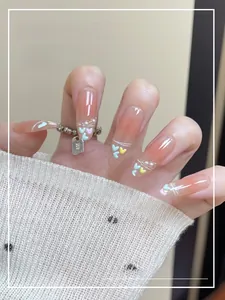 Detail of pink gradient press-on nails with heart charms and white pearls on almond shape