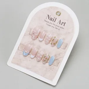 Press-on nail set featuring French tips, bow designs, and blue floral nail art on a card