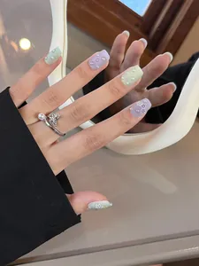 Detalle de uñas postizas de flores macaron con perlas 3D y un anillo de mariposa