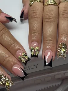 Close-up of black French tips with 3D gold glitter bows and sparkling rhinestone accents