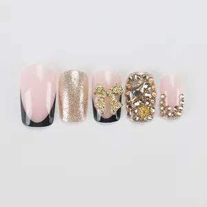 Detail of press-on nails featuring black French tips, golden bows, and rhinestones