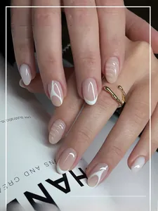 Macro shot of short oval French press-on nails with nude pink base and white spiral wave patterns