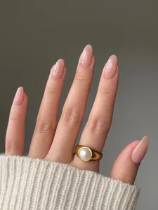 Detail of wide gold ring with white pearl worn with gradient nude manicured nails