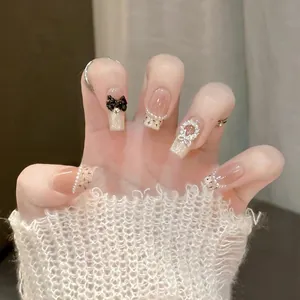 Detail of luxury press-on nails with 3D black bows, pearls and golden cat-eye finish