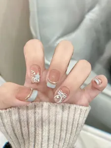 Detail of handmade short press-on nails with blue French tips and white 3D bows
