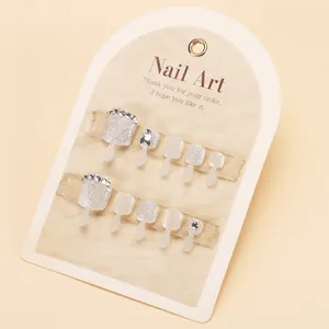Silver glitter and milky white press-on toenails with diamond accents on cardboard