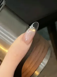 Detail of nude gradient press-on nails with silver flower charm and elegant white dots