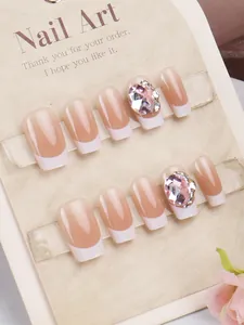 Detail van handgemaakte kunstnagels met witte French tips en roze strass-steentjes