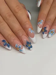 Detail of almond-shaped nails with blue floral designs, white tips and gold beads