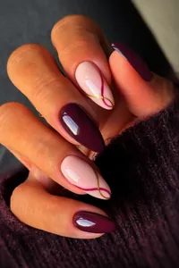 Detail of almond-shaped press-on nails with wine red polish and gold wavy stripes