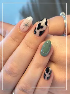 Macro detail of long oval press-on nails with cow print, star charms and metallic lines