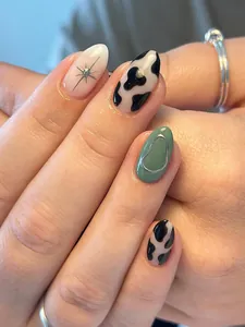 Detail of almond-shaped press-on nails with cow print and 3D metallic star accents