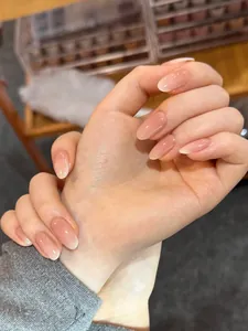 Glossy nude pink gradient almond shape press-on nails shown on hands in a natural setting
