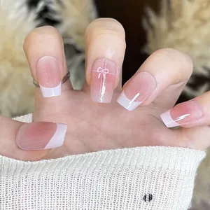 Detail of French nude pink gradient press-on nails with white bows and glitter finish