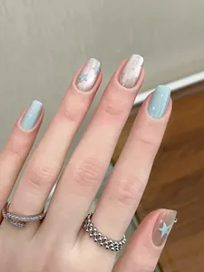 Close-up of blue cat-eye press-on nails with star patches and silver rings detail