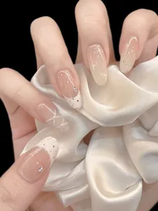Close-up of nude and white press-on nails with delicate pearl accents and bow details