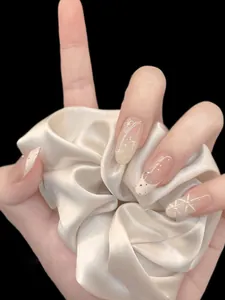 Detail of nude almond press-on nails with bow design and satin scrunchie accessory