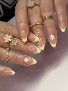 Primer plano de uñas postizas almendradas color rosa nude con puntas amarillas y margaritas