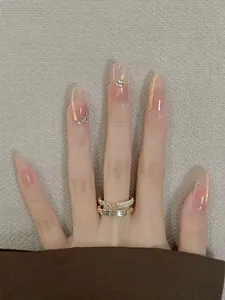 Macro detail of nude gradient almond nails with rhinestones and gold screw motif rings
