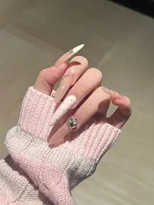 Macro detail of long stiletto press-on nails with nude pink crystals and black polka dots