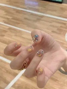 Detail of short pastel pink press-on nails with yellow stars and colorful rhinestones