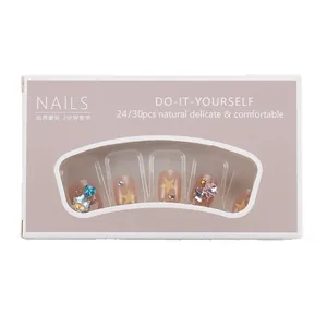 Short nude pink press-on nails with yellow stars and colorful rhinestones in a box