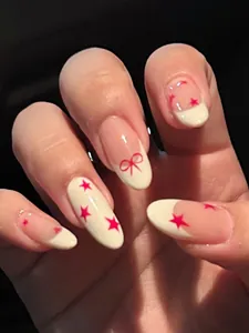 Close-up of oval press-on nails with red stars and a bow on creamy white base