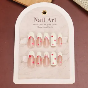 Pink French almond press-on nails with red stars and bow-knot designs on display card