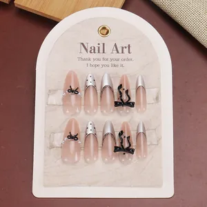 Long almond press-on nails with black lace, pearls, and bows on nude pink base