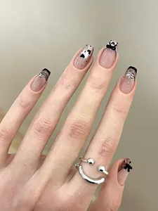 Detail of nude pink press-on nails with black French tips, bows, and a silver smiley ring