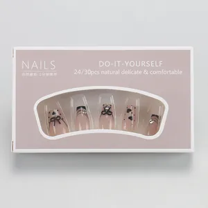 Detail of boxed press-on nails featuring nude gradient, black bows, and rhinestone accents
