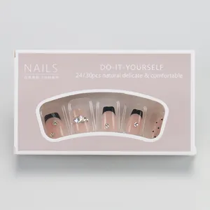 Detail of pink press-on nails with black French tips, polka dots and rhinestones