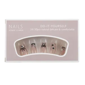 Short trapezoid press-on nails set with nude gradient, black bows, and heart rhinestone accents