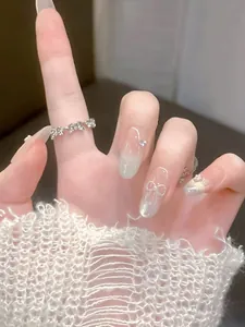 Close-up of pink press-on nails with white 3D bows and sparkling silver rhinestones