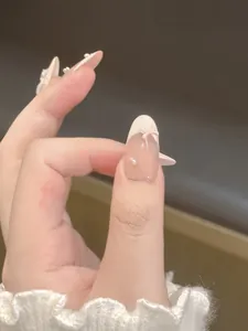 Close-up of almond-shaped press-on nails with nude pink base, white French tips and bows