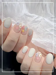 Gros plan de faux ongles courts ovales avec de douces fleurs roses et blanches peintes à la main