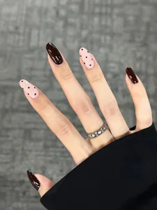 Dettaglio di unghie finte ovali in marrone scuro e rosa chiaro con motivi a pois neri