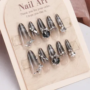 Detail of handmade silver-black cat eye press-on nails with rhinestones and bow charms
