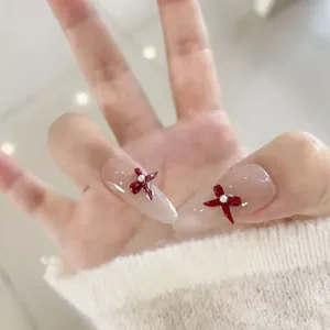 Lange Stiletto Kunstnägel in Nude-Rosa mit roten Schleifen und weißen Perlen