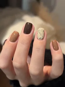 Short square press-on nails in earthy brown and cream with black ink-splatter detail