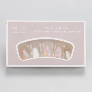 Détail de faux ongles ovales roses et blancs avec motifs floraux dans leur emballage