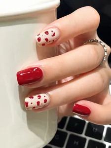Detailed view of red and polka dot press-on nails on hands holding a white ceramic mug