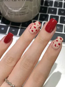 Short square press-on nails featuring red and white cow print patterns in a lifestyle setting