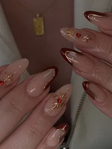Detail of almond-shaped nails featuring nude pink, deep red, and gold embossed floral art