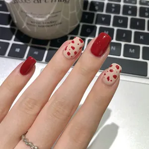 Short red and spotted almond press-on nails shown against a stylish office laptop setup